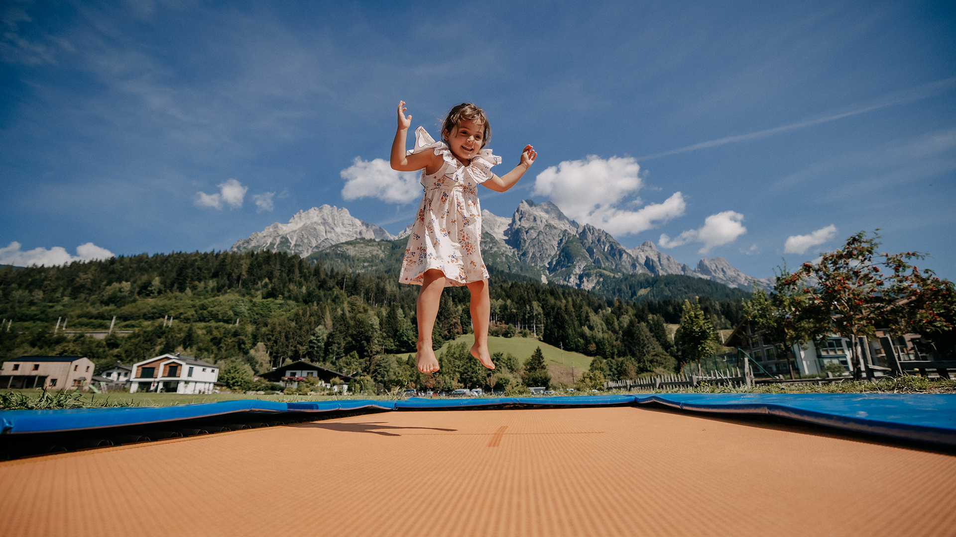A girl jumps joyfully on a large trampoline, enjoying the view of the Leogang Mountains.