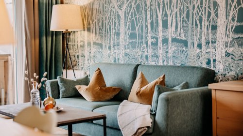 Türkise Couch mit gelben Zierkissen, links befindet sich eine Stehlampe.