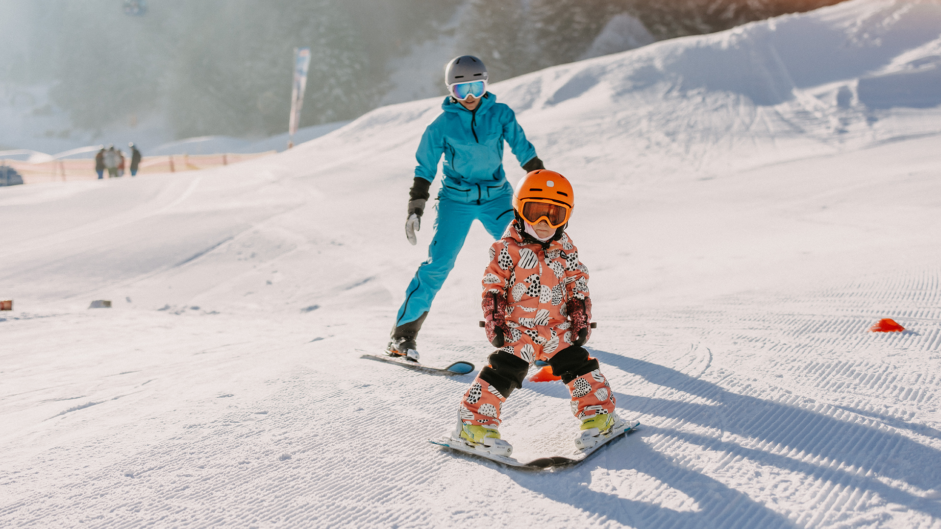 Eine Mutter fährt mit ihrem Kind im Schnee am Übungshang in Leogang Ski.