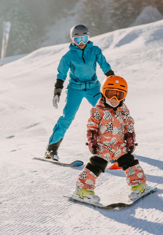 Eine Mutter fährt mit ihrem Kind im Schnee am Übungshang in Leogang Ski.