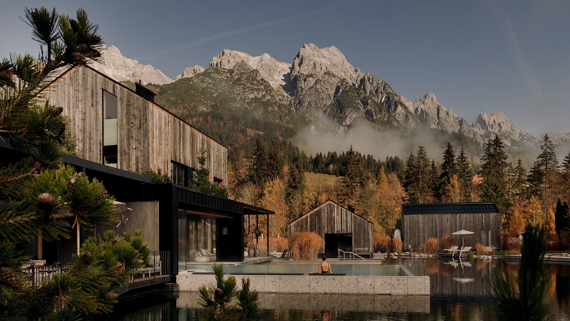 Blick auf die Seesauna und den beheizten Außenpool „Seepool“ im Forsthofgut, umgeben von bunten Herbstbäumen und Bergpanorama.