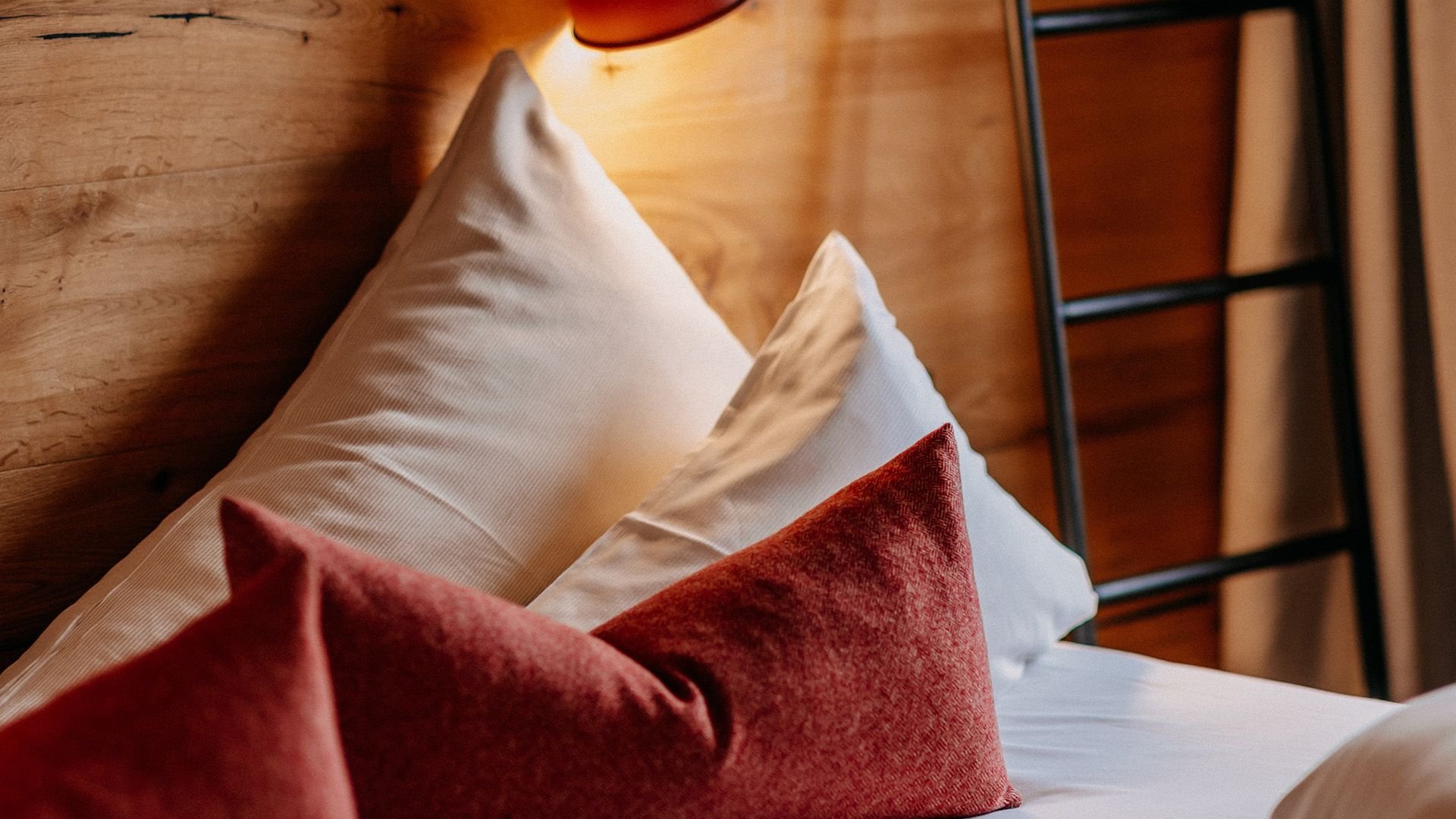 Close-up of a cozy bed with red decorative cushions and white bedding.
