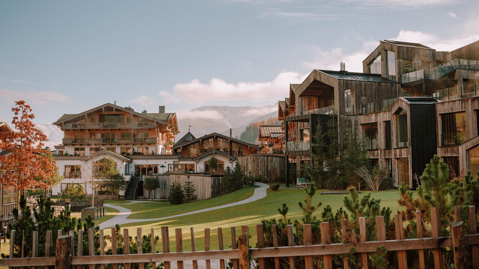 Blick auf das Naturhotel Forsthofgut mit moderner Holzarchitektur, Garten und umliegenden Bergen im Hintergrund.