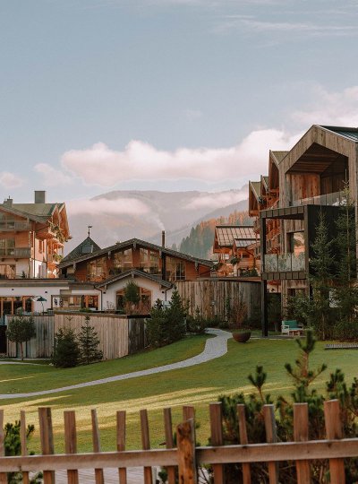 Blick auf das Naturhotel Forsthofgut mit moderner Holzarchitektur, Garten und umliegenden Bergen im Hintergrund.