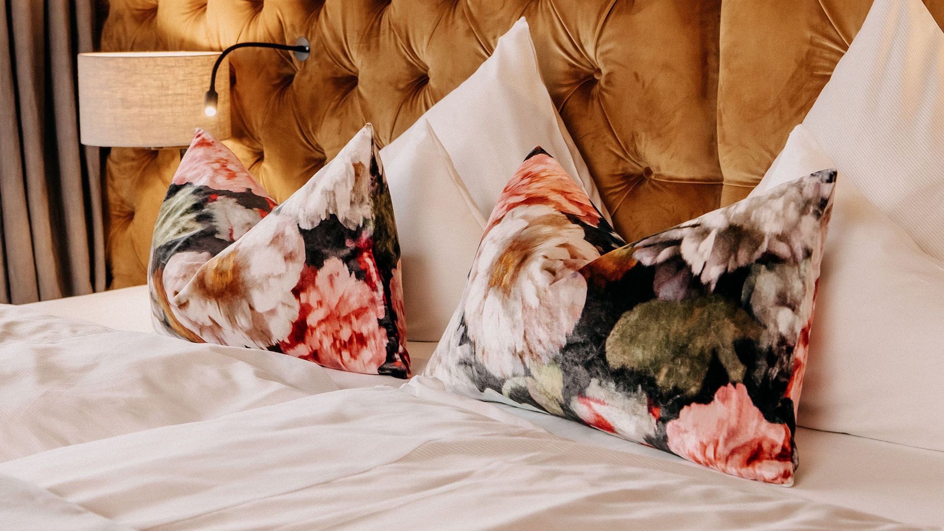 Close-up of a bed with decorative pillows and a bedside lamp.